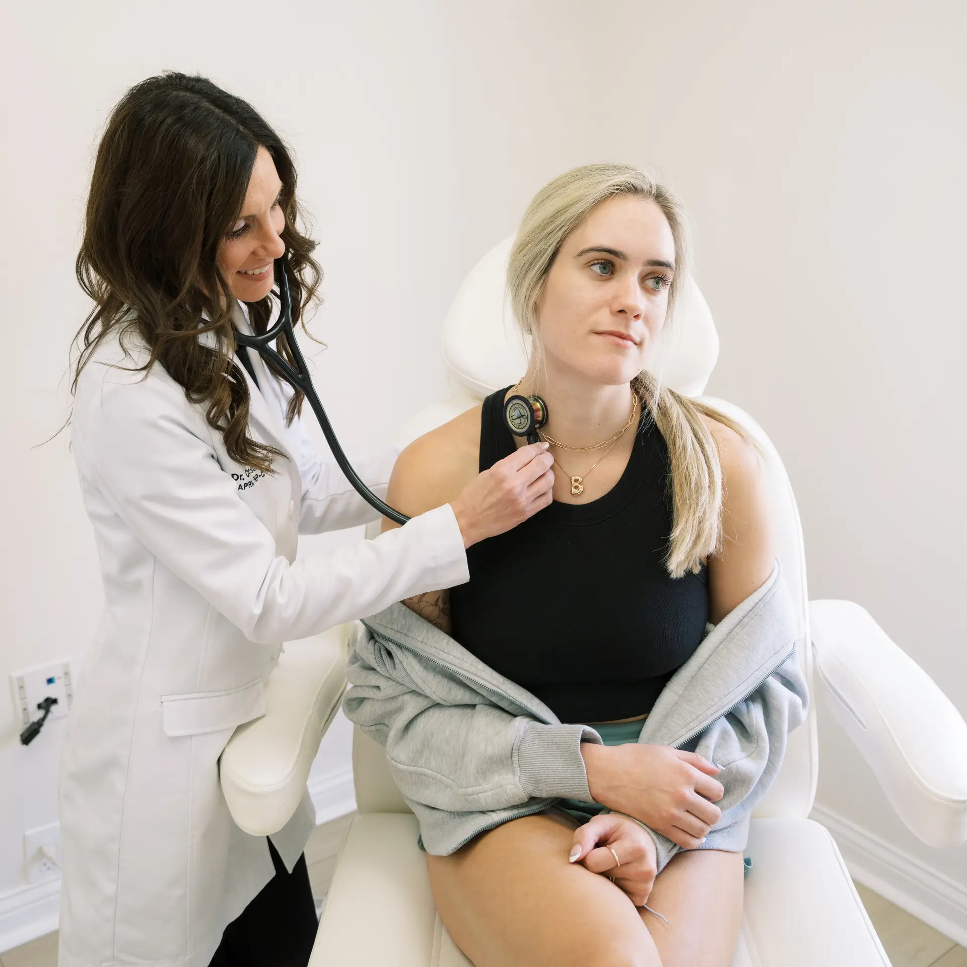 Doctor in a white coat using a stethoscope to check a patient's heartbeat in a clinic.